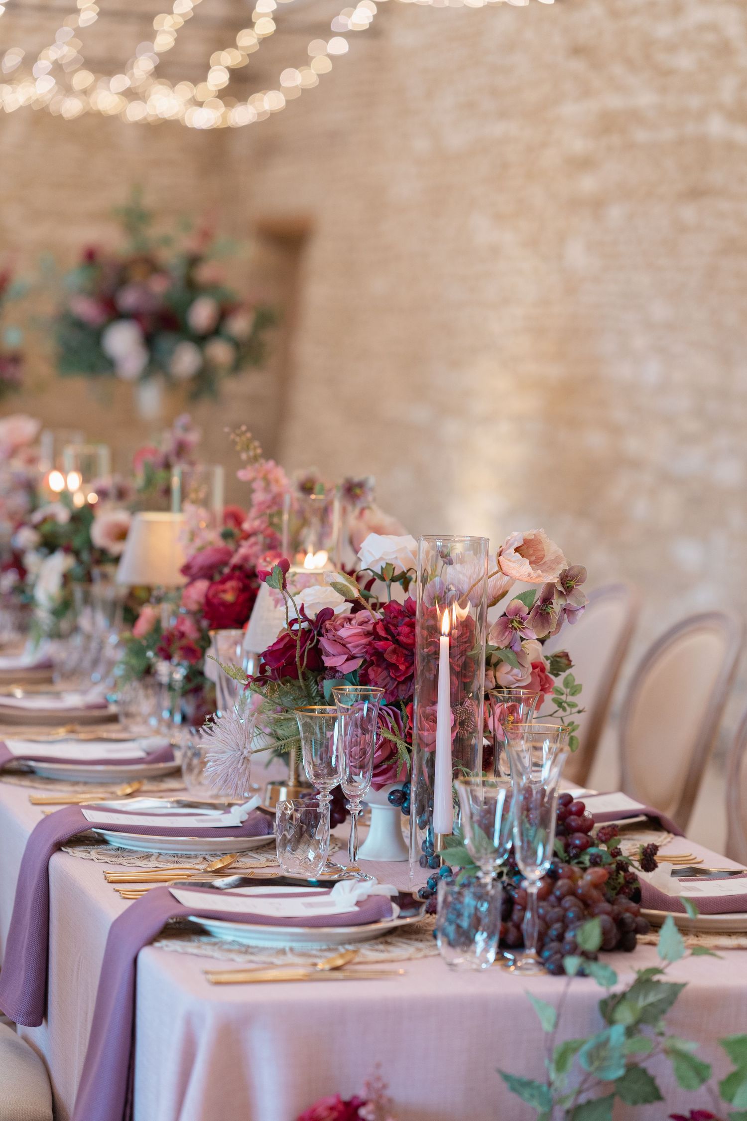 Elegant wedding table setting with pink and burgundy florals and purple accents.