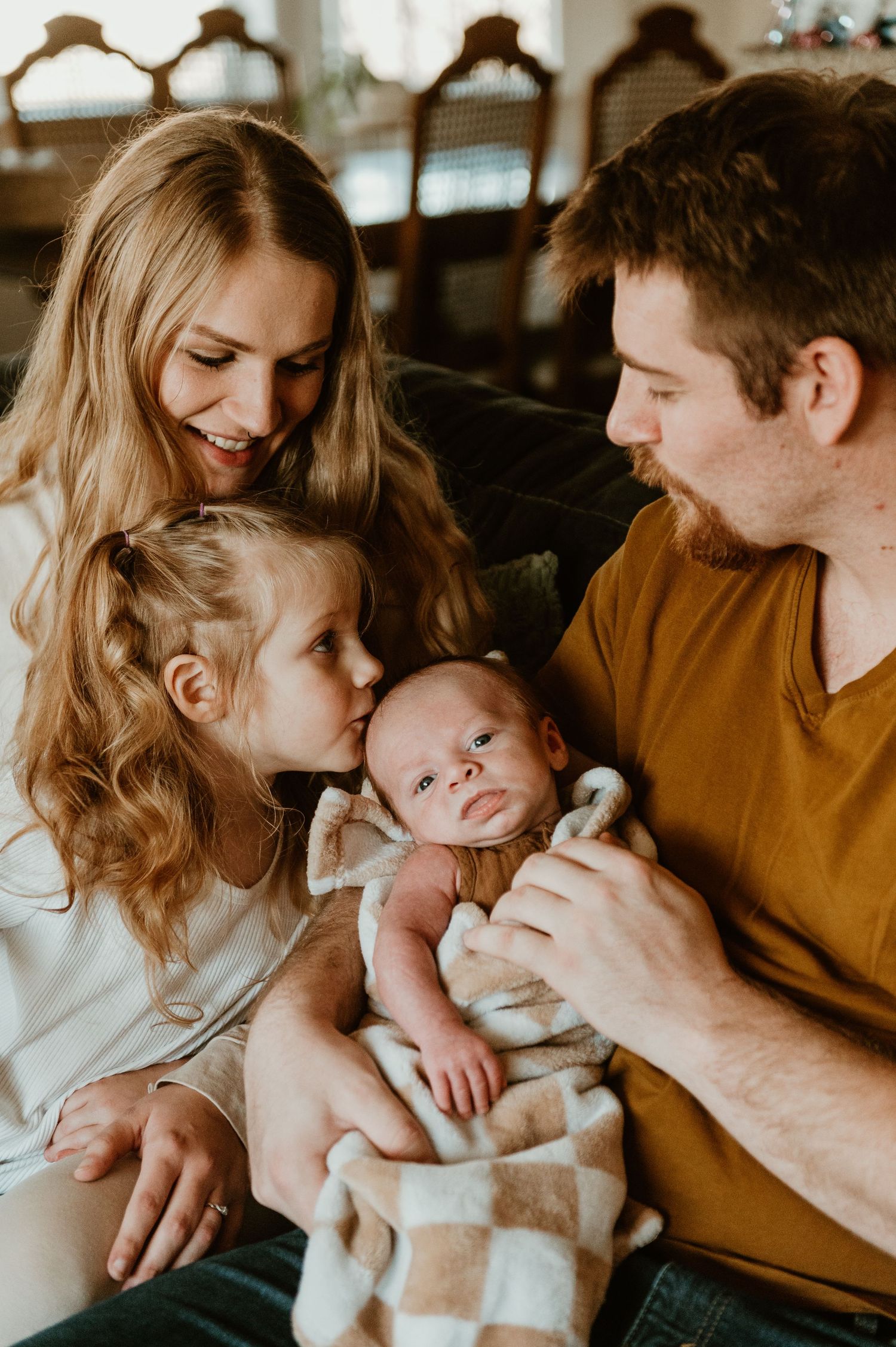 Intimate family moment as parents and young daughter bond with newborn baby on couch at home.