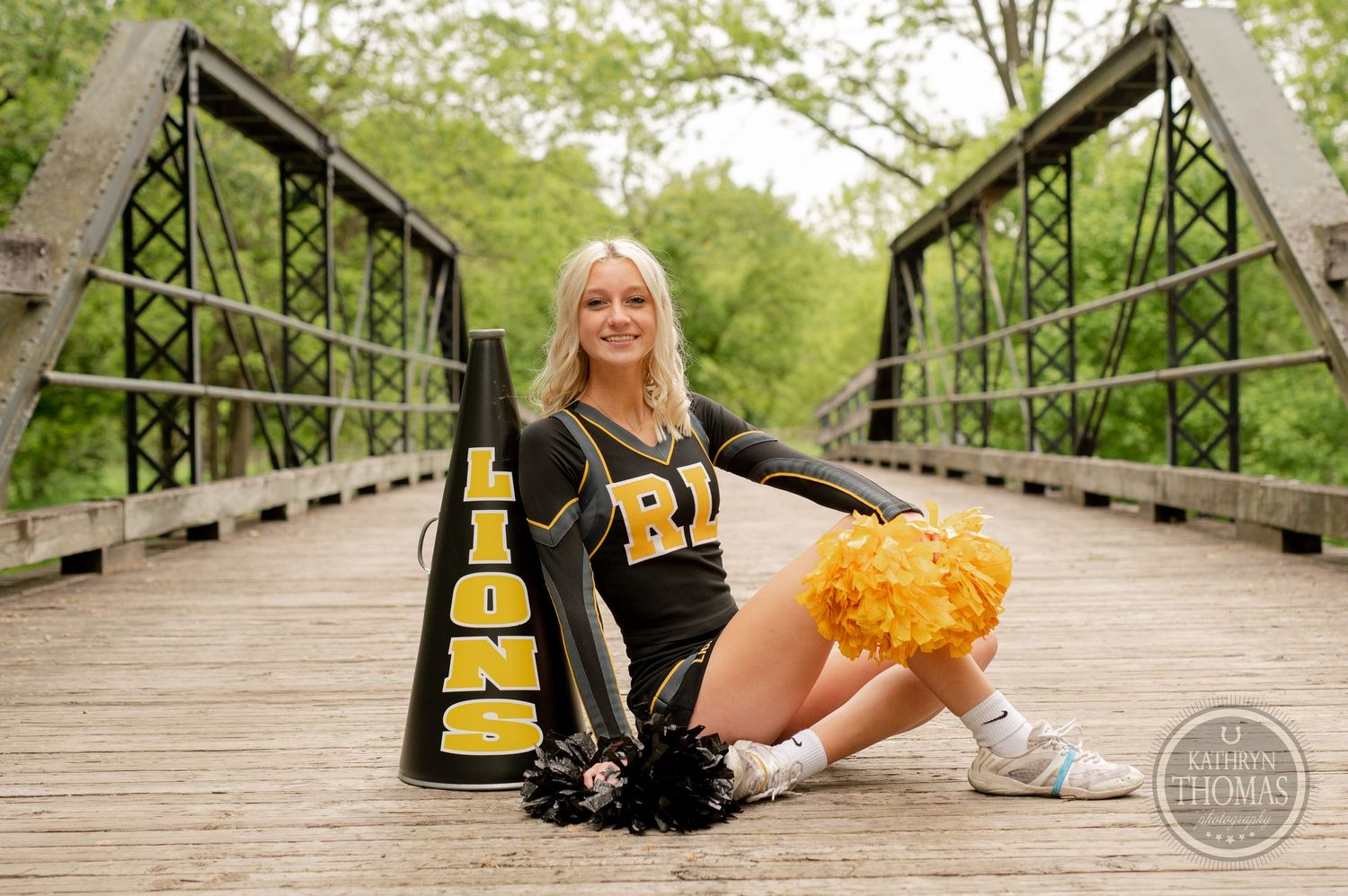 Cheerleader posing with megaphone and pom poms on wooden bridge.