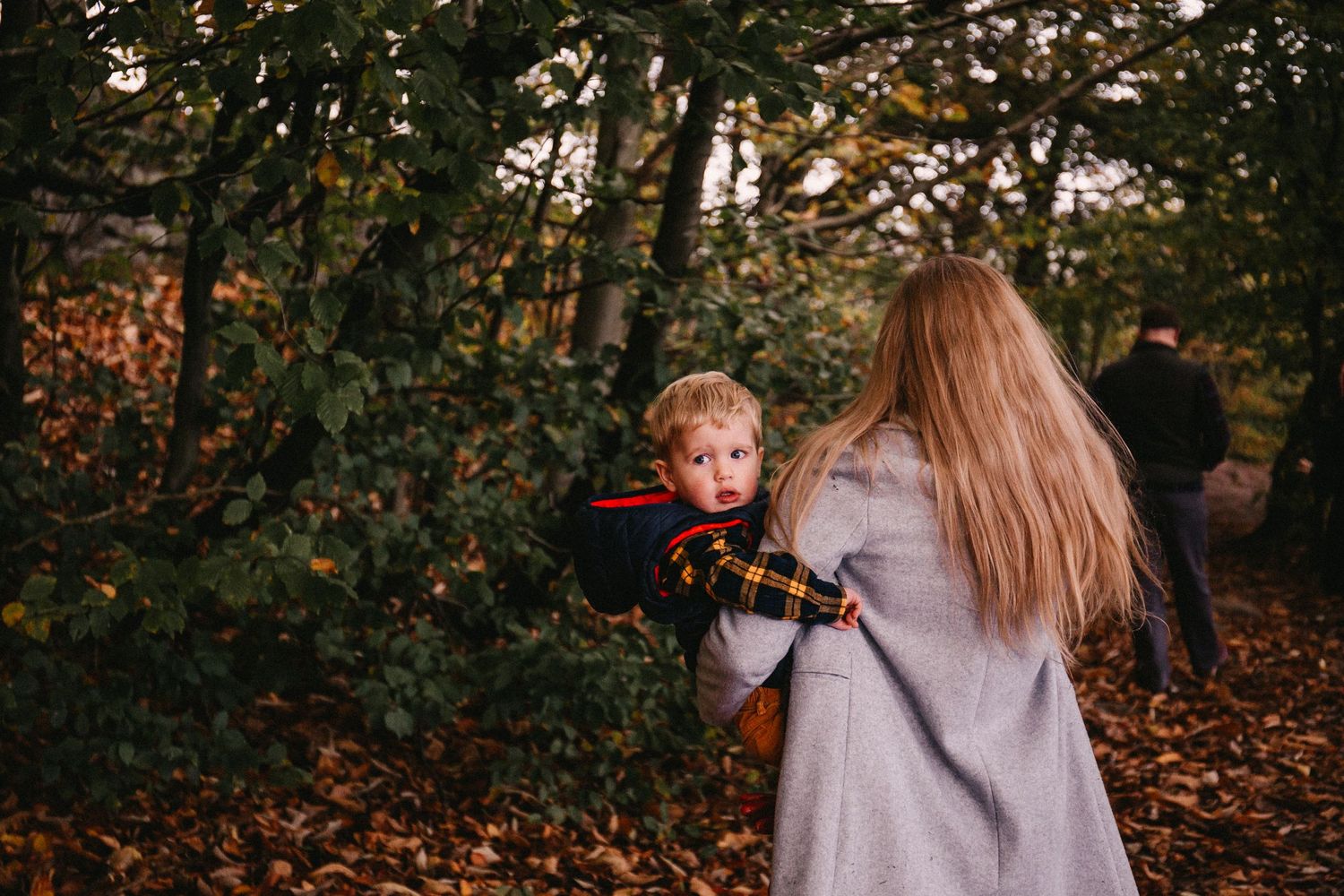 A candid autumn photography session in a wooded area with fallen leaves.