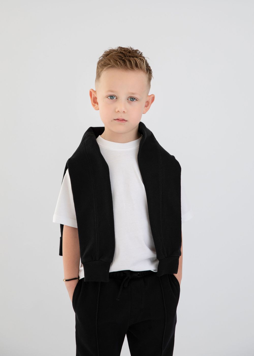 Fashion portrait showing black vest and white t-shirt ensemble against white backdrop.