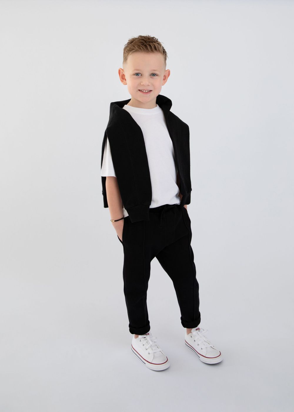 Model wearing black athletic outfit and white sneakers poses in studio setting.