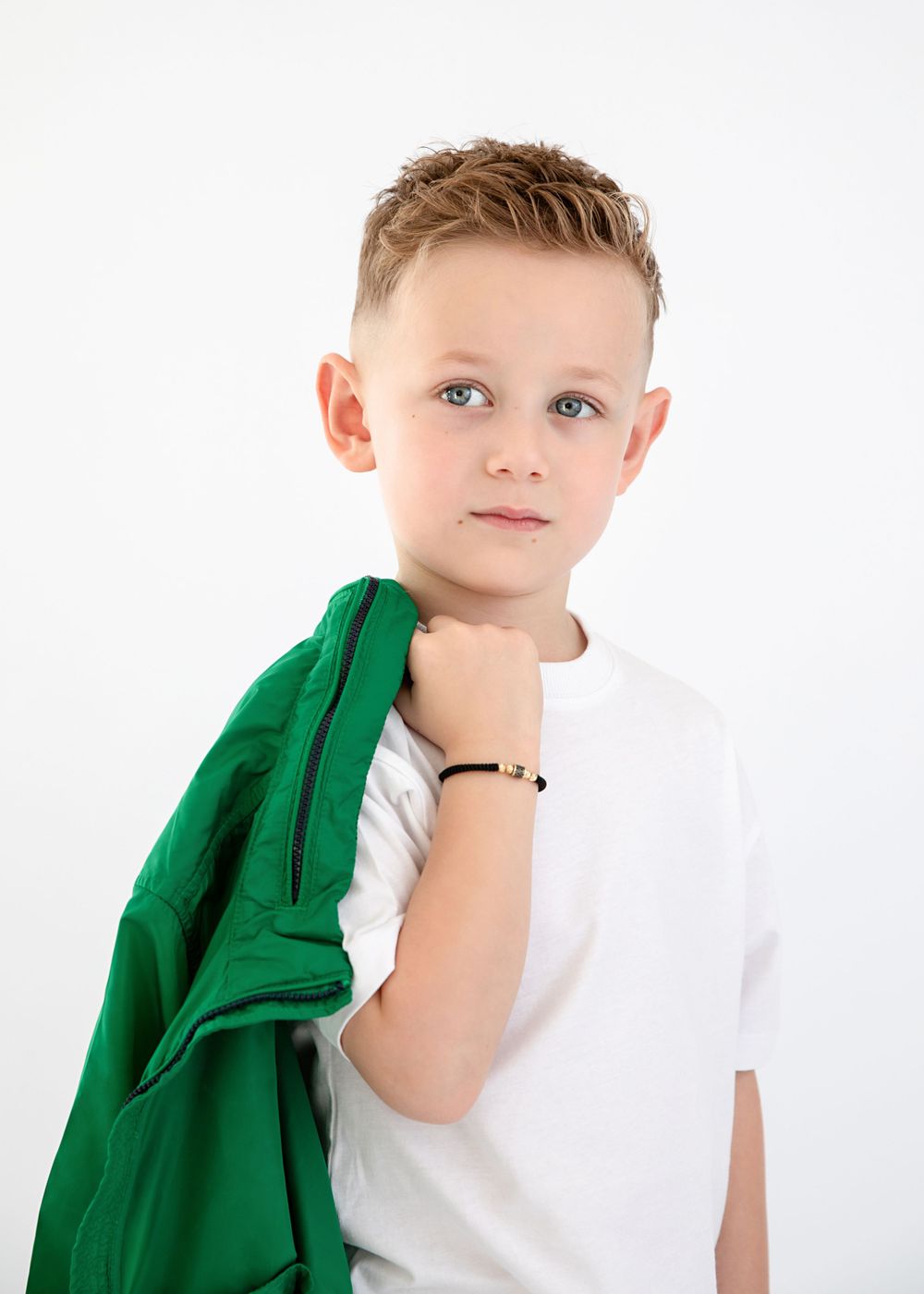 Studio portrait featuring white t-shirt and green jacket against minimalist background.