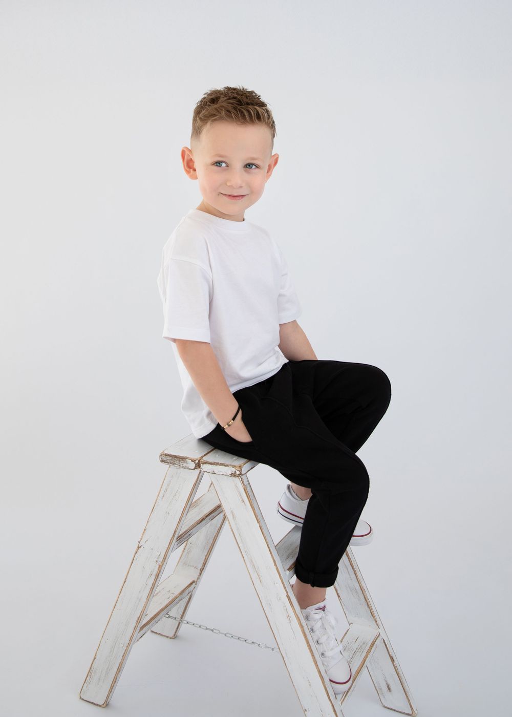 Casual portrait of model seated on white ladder wearing monochrome outfit.