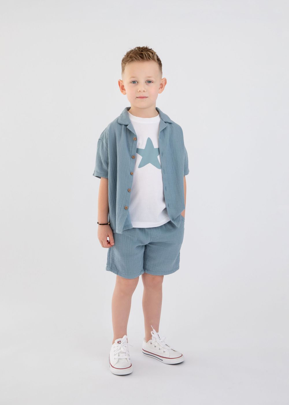 A child in a light blue coordinated outfit with white sneakers stands against a white backdrop.