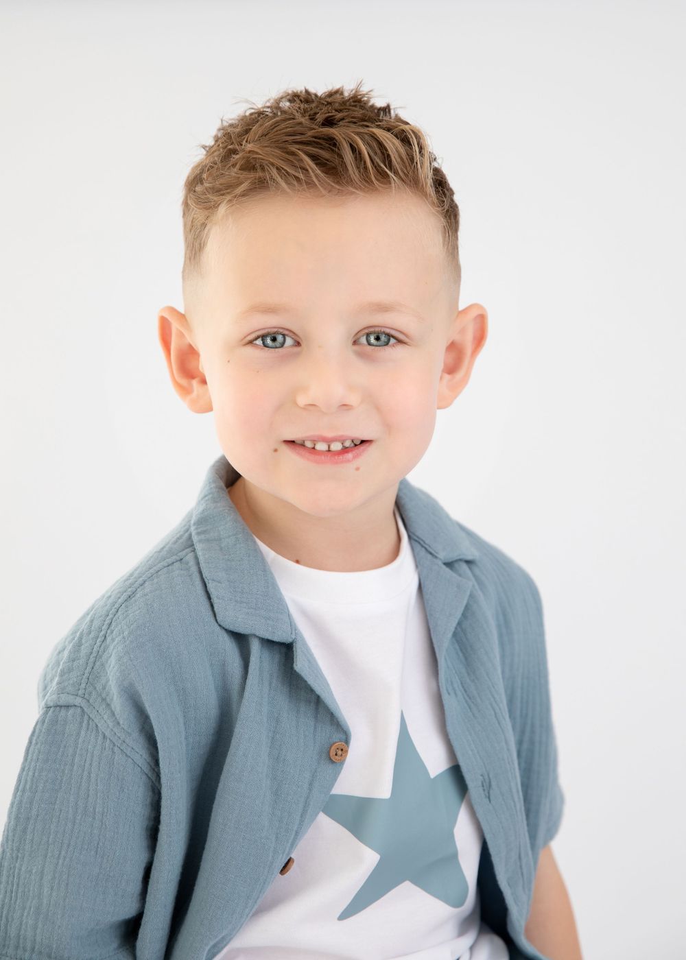 Portrait of model in light blue jacket with star print t-shirt against white background.