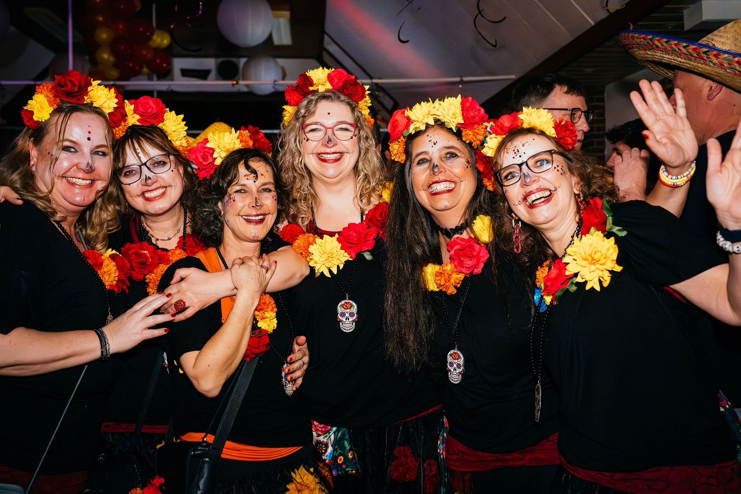 Group of women wearing matching orange party hats and carnival costumes, smiling and waving at a vibrant event. birthday party Straelen