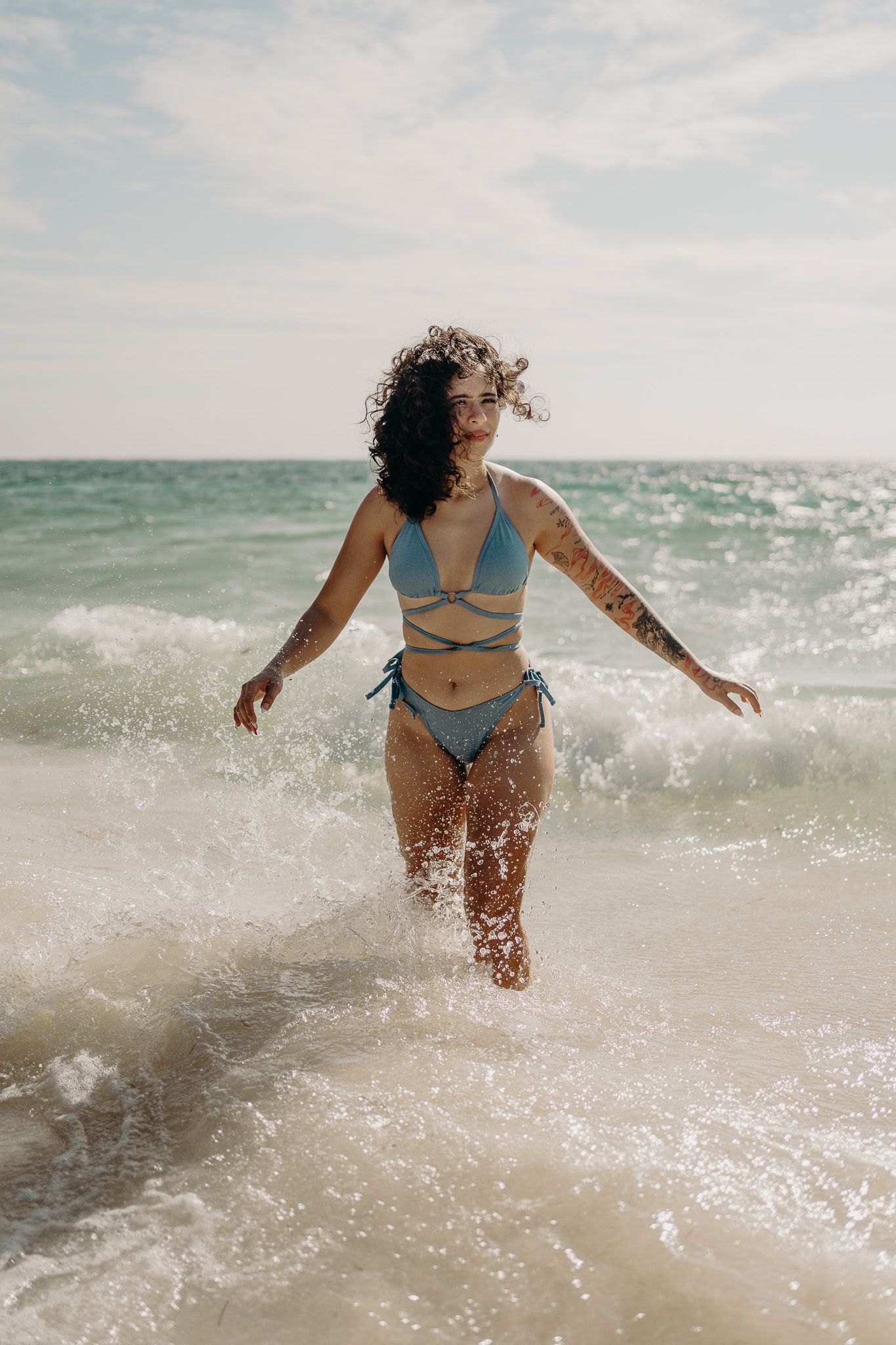 Woman in blue strappy bikini playing in ocean waves on sunny beach photoshoot in Puerto Morelos.