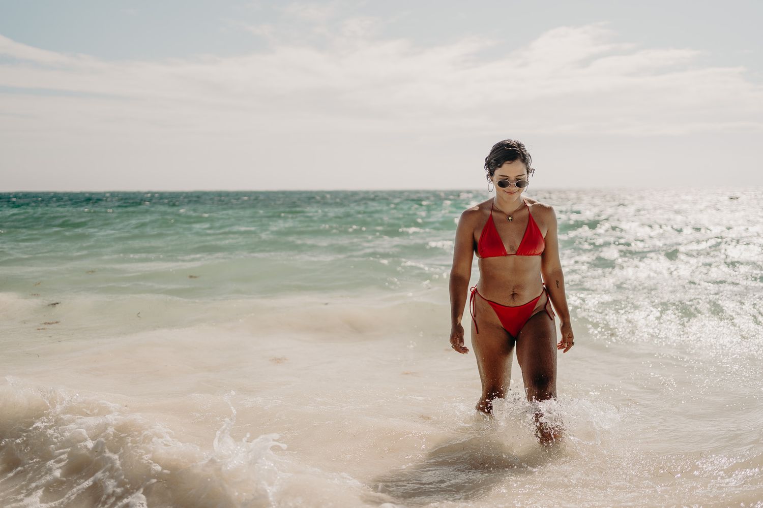 Figure in red bikini standing in ocean waves on a beautiful beach day photoshoot in Puerto Morelos.