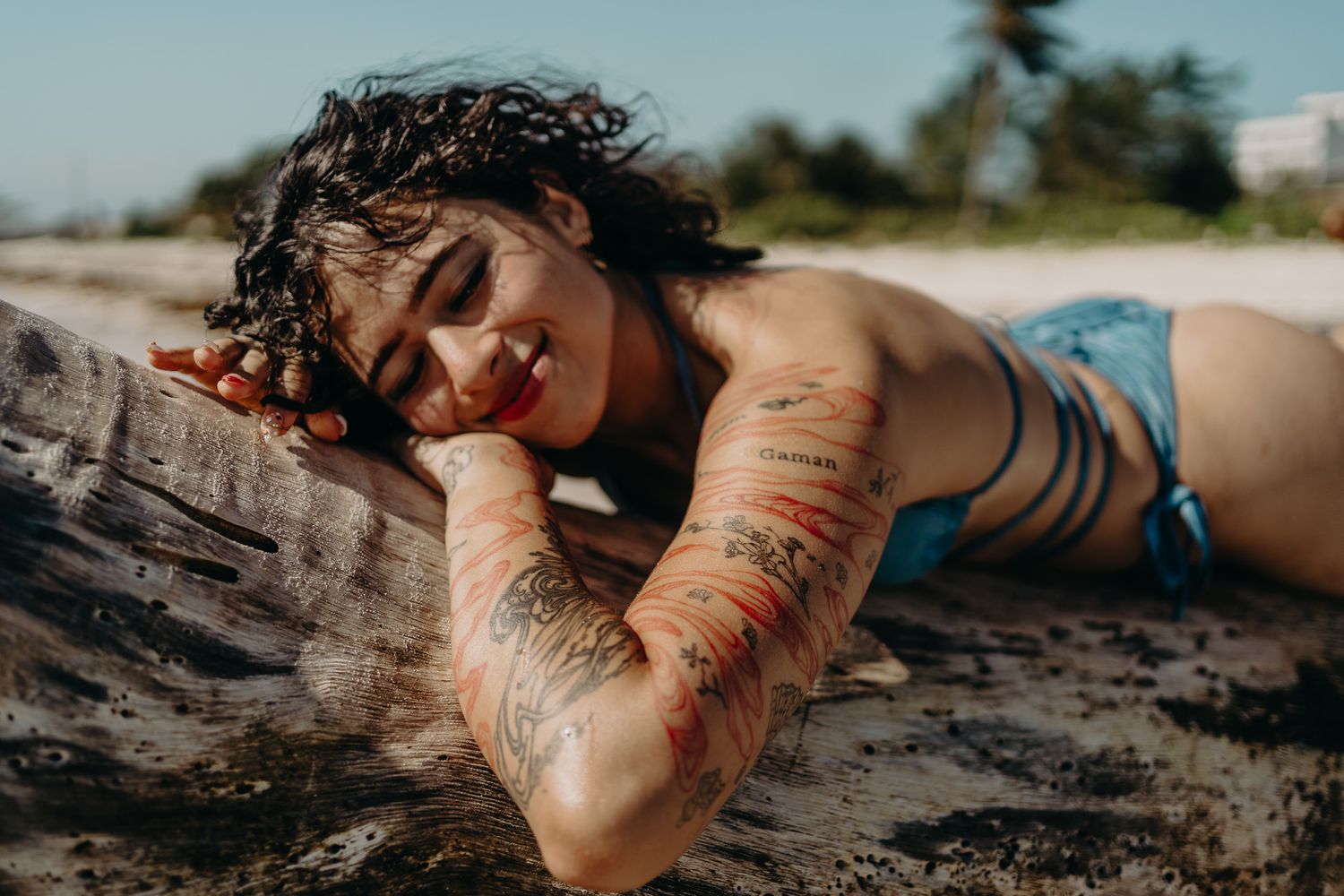 Person with tattoo sleeve relaxing on driftwood at the beach photoshoot in Puerto Morelos.