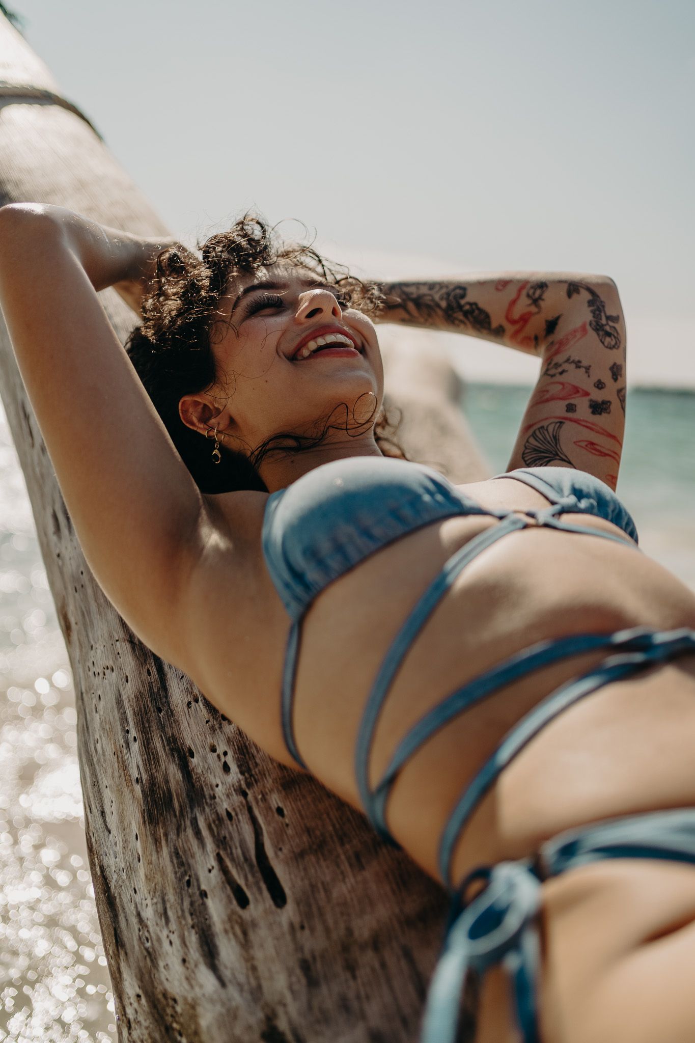Person relaxing on driftwood log at beach wearing blue swimwear photoshoot in Puerto Morelos.