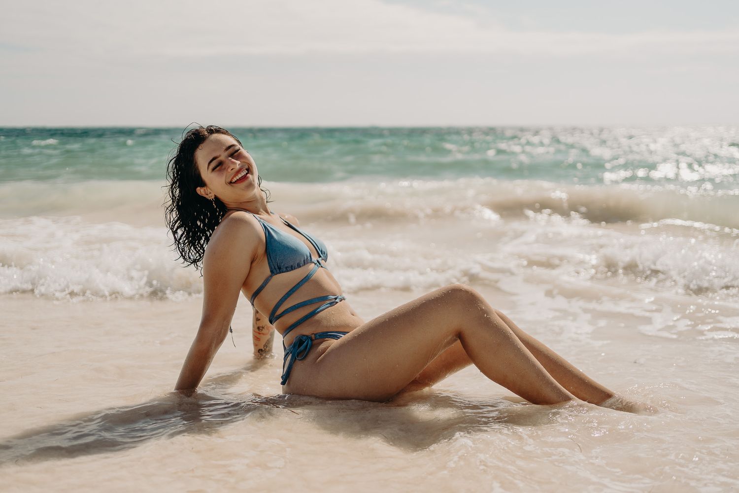 Carefree moment at the beach in blue bikini with ocean waves behind photoshoot in Puerto Morelos.