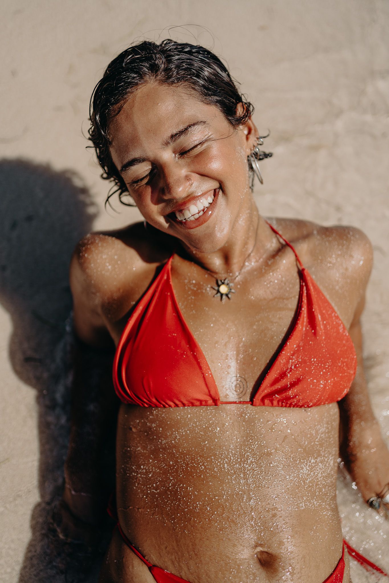 Woman in a red bikini lounging on a sandy beach in bright sunlight photoshoot in Puerto Morelos.