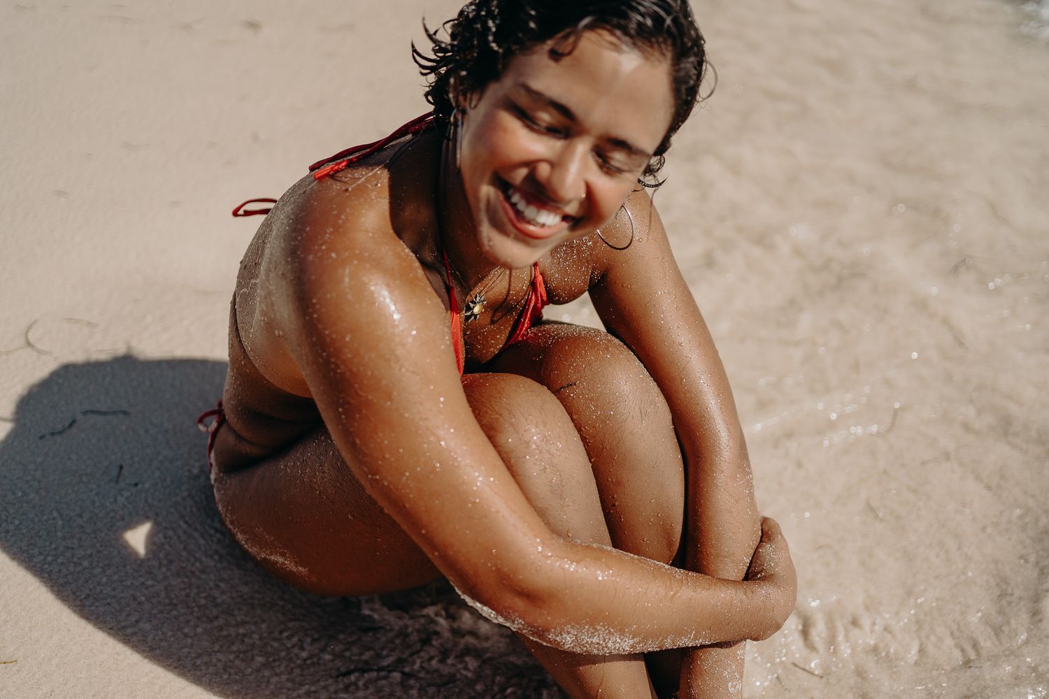 Woman lying on beach sand wearing a bright red swimsuit photoshoot in Puerto Morelos.