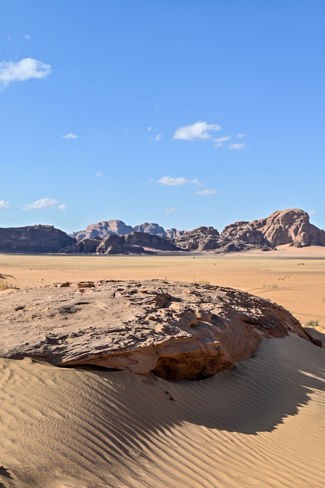Desert sand dunes and rock formations under bright blue sky in Wadi Rum.