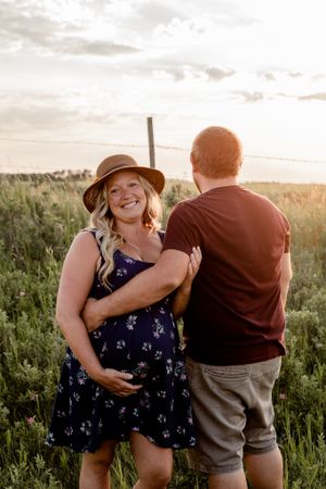 pregnant woman facing forward with husbands arm wrapper around her belly