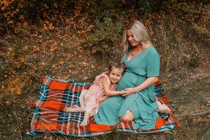 toddler and mother sitting on blanket, daughter is hugging moms pregnant belly