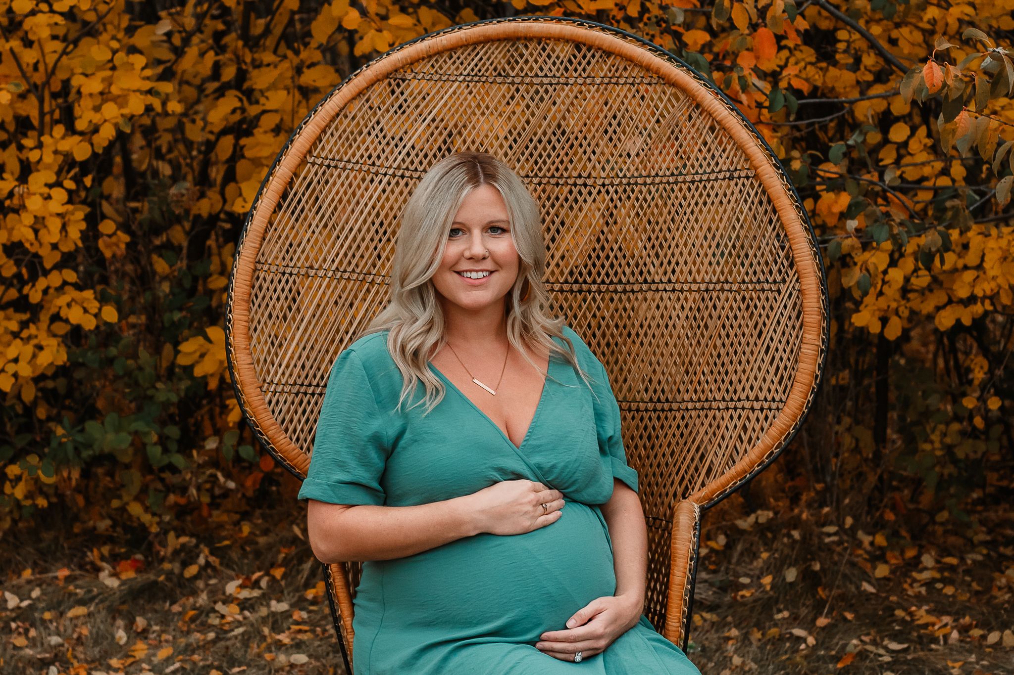 pregnant mama sitting on peacock chair with fall leaves behind her