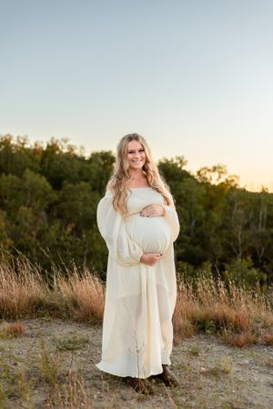mama holding pregnant belly at sunset
