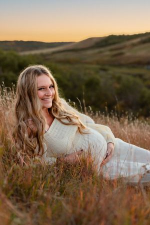 Pregnant woman cradling her belly in valley at sunset