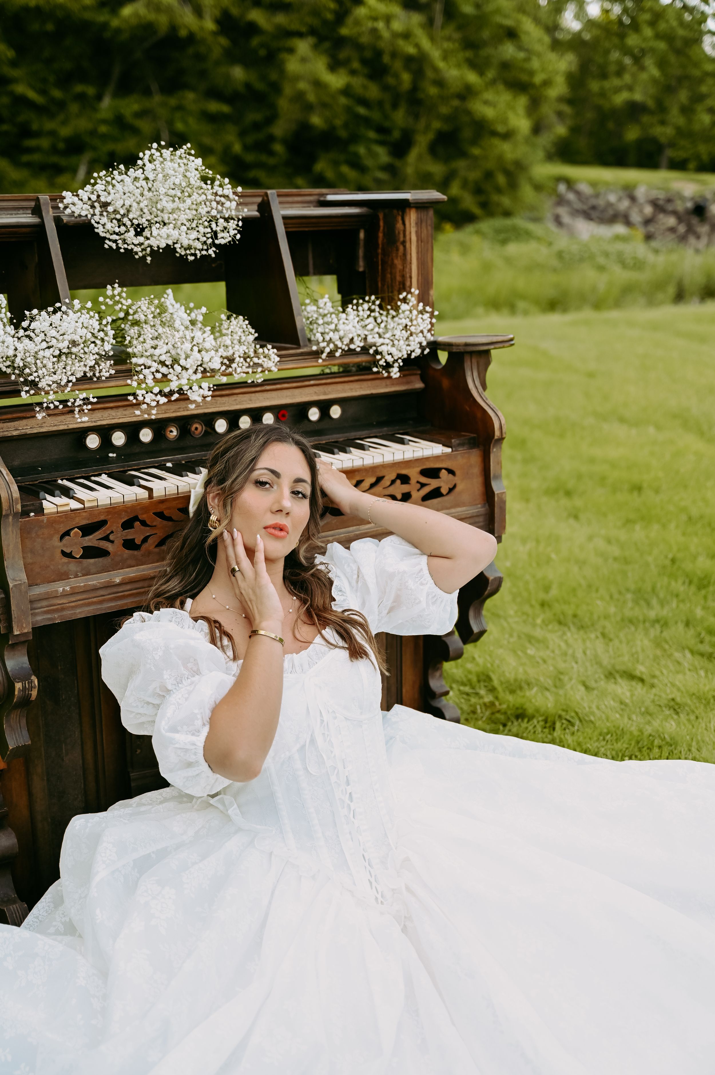 Elegant white wedding dress flowing across a vintage piano outdoors in a lush green garden setting.