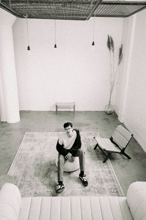 Black and white interior photo showing a minimalist room with hanging lights, benches, and a rug on concrete floor.