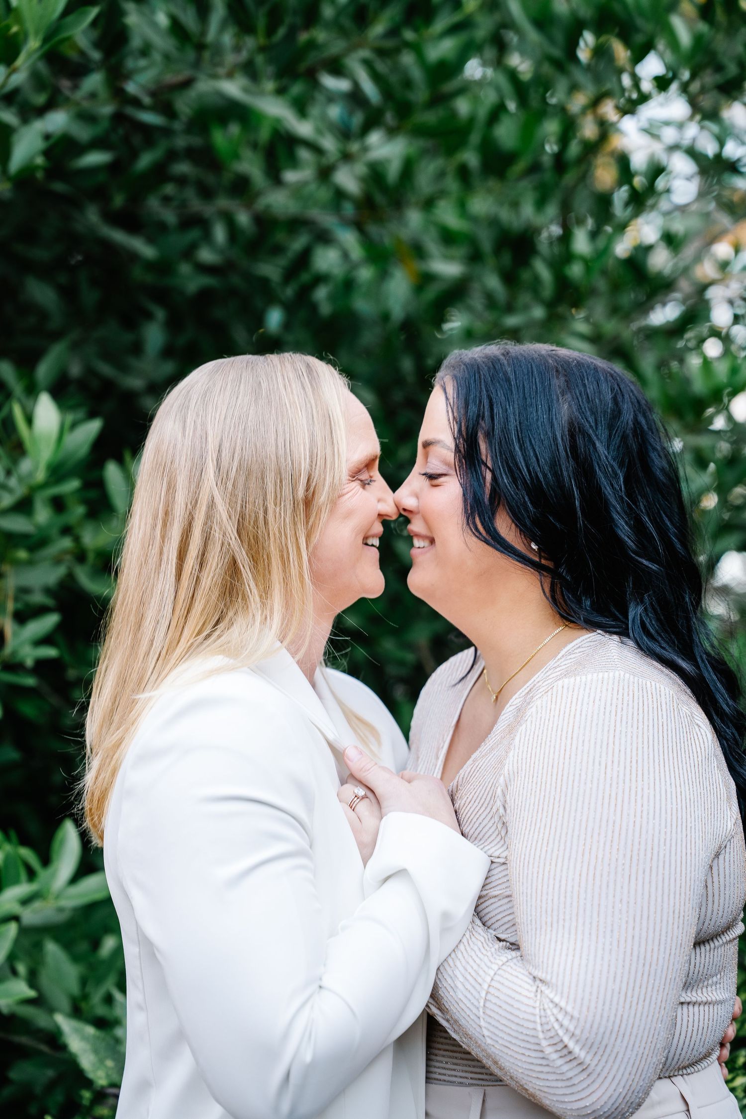 Brides sharing a smiling kiss against a luscious green tree during a wedding ceremony at Weymouth Center for Arts and Humanities in NC.