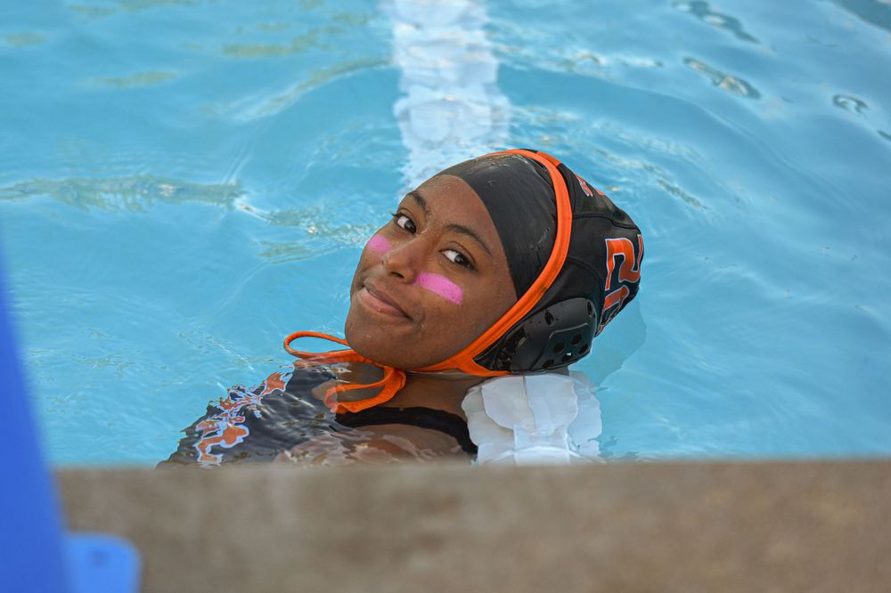 Water polo athlete in protective cap emerges from pool during competitive match.