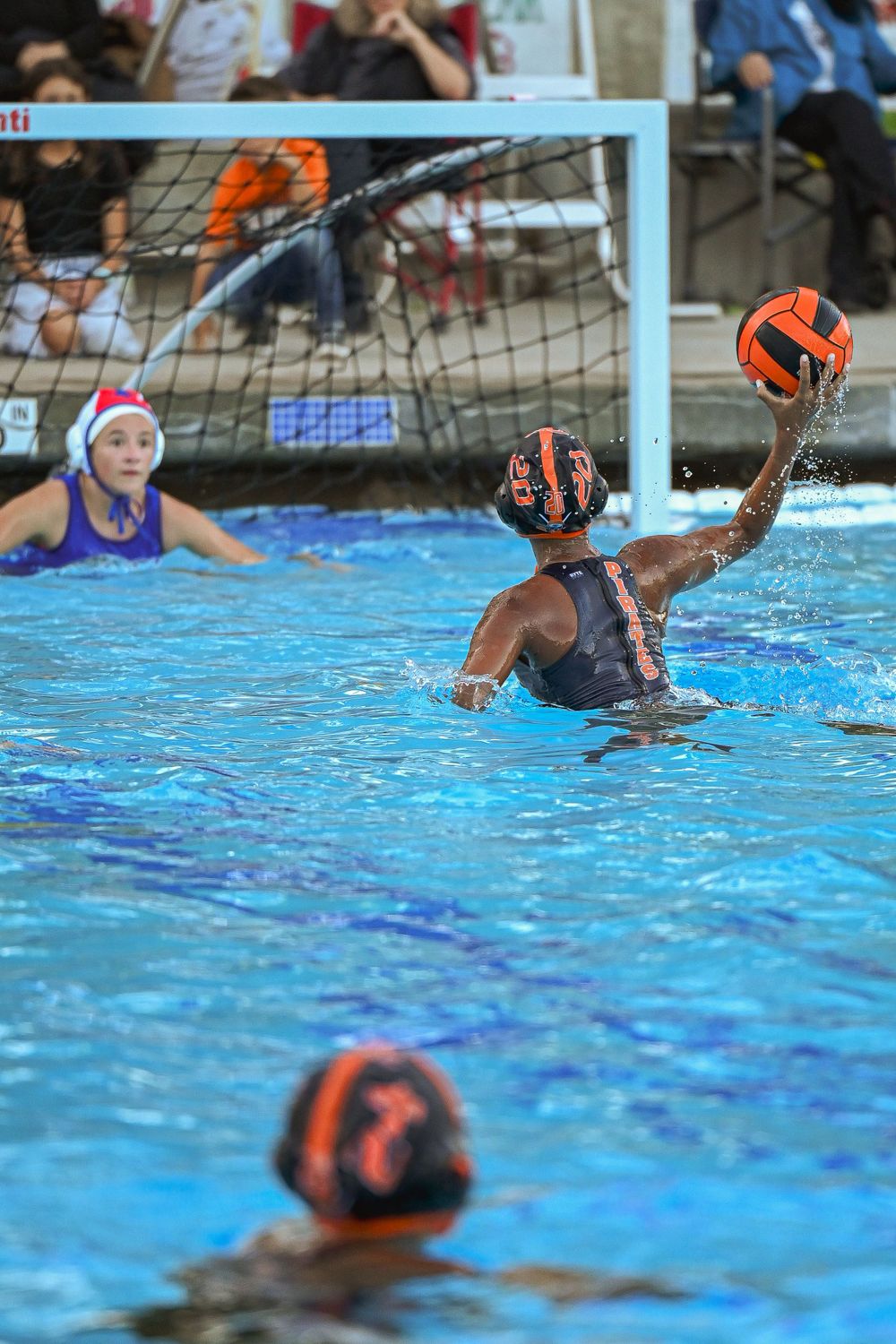 Water polo goalie defends goal during competitive match in swimming pool.