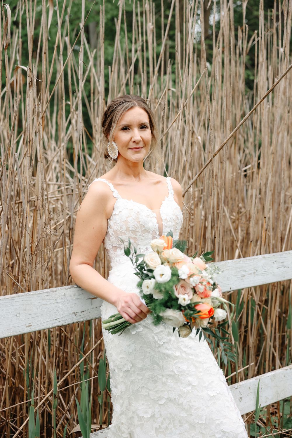 A romantic bridal photo featuring a delicate bouquet of peach and white flowers against dried reeds.