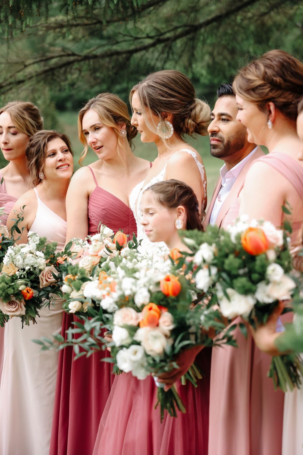 Wedding party members hold beautiful peach and white flower bouquets while smiling outdoors.
