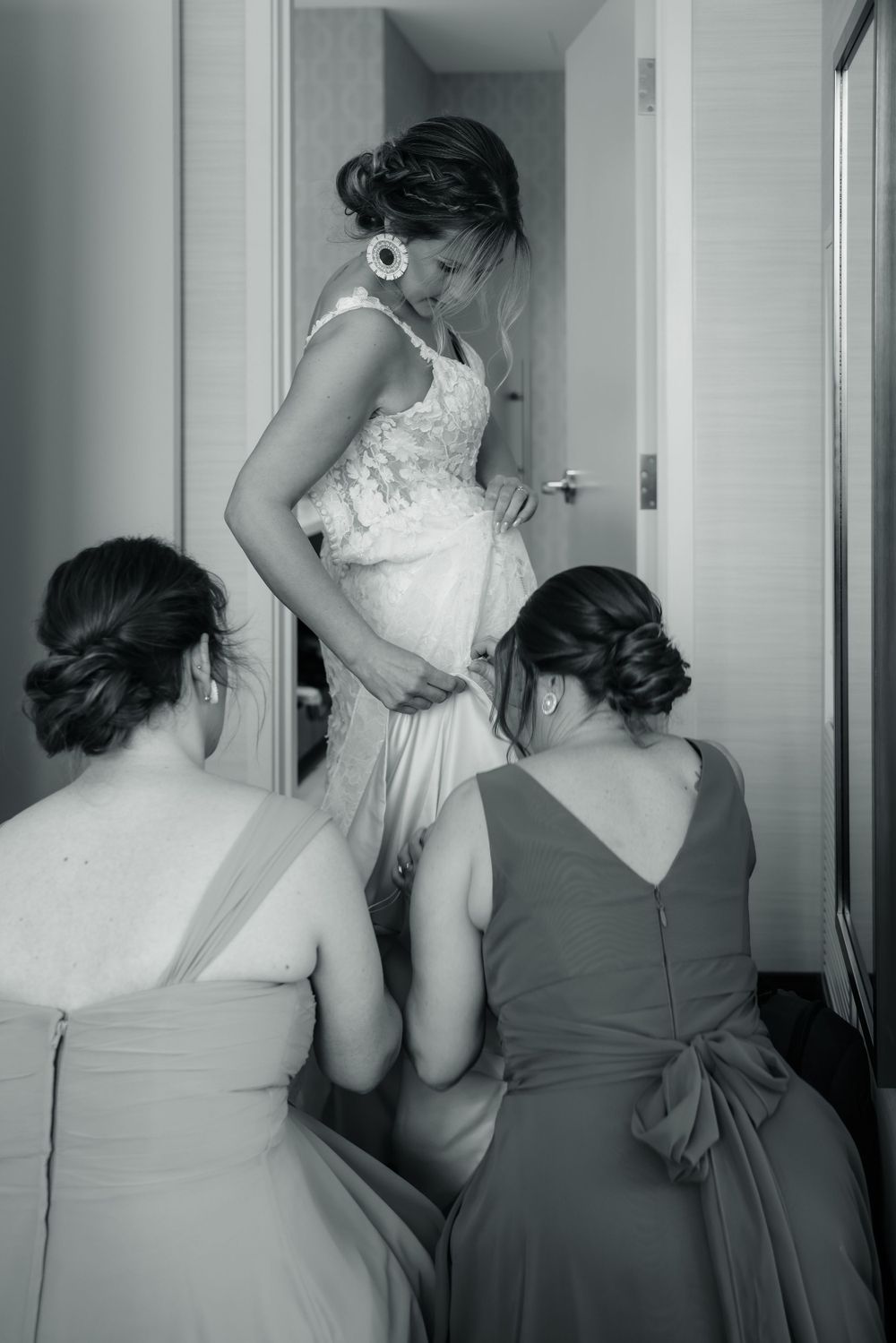 Wedding dress being adjusted by bridesmaids in black and white photograph.