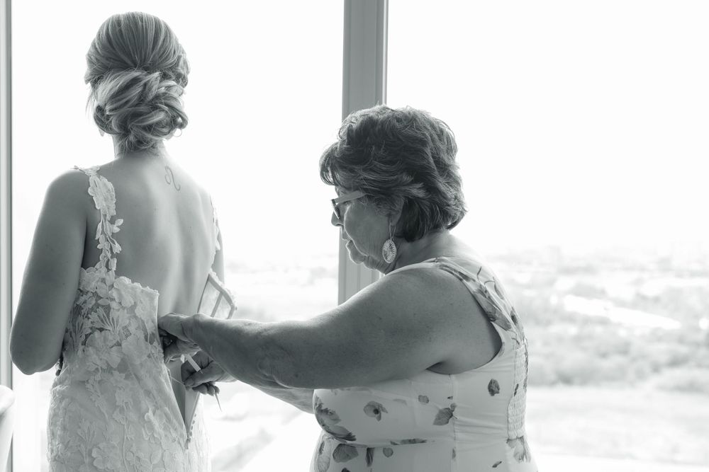 A tender moment of wedding dress preparation by a window with delicate lace details being adjusted.