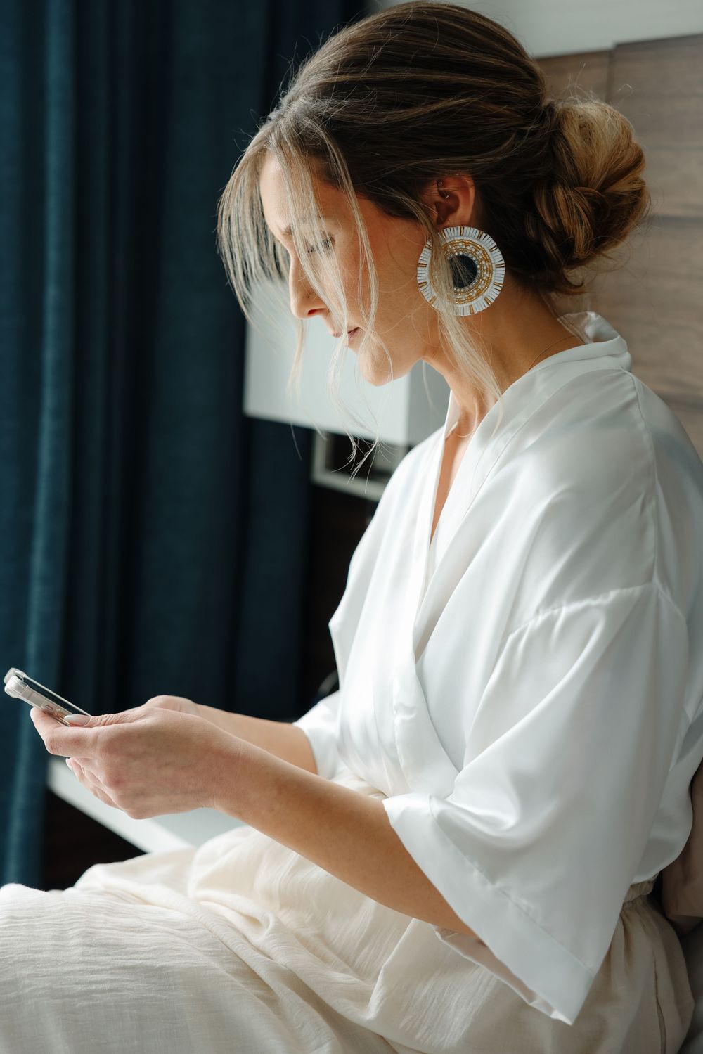 Side profile of person wearing statement earrings and white robe checking phone.