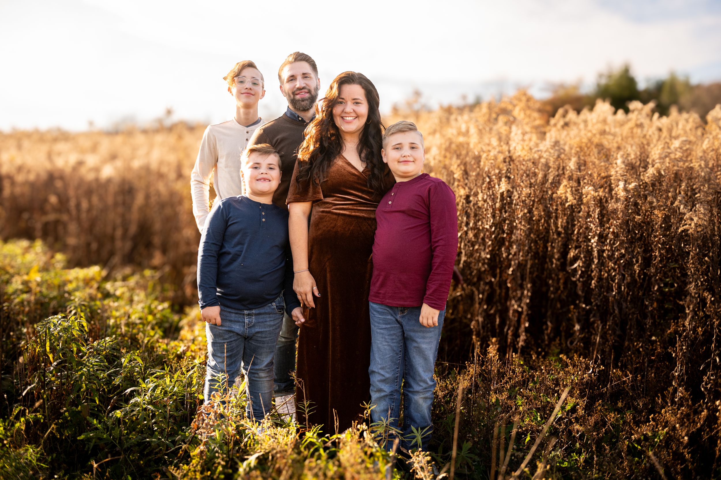 A family stands together in a golden field at sunset during autumn.