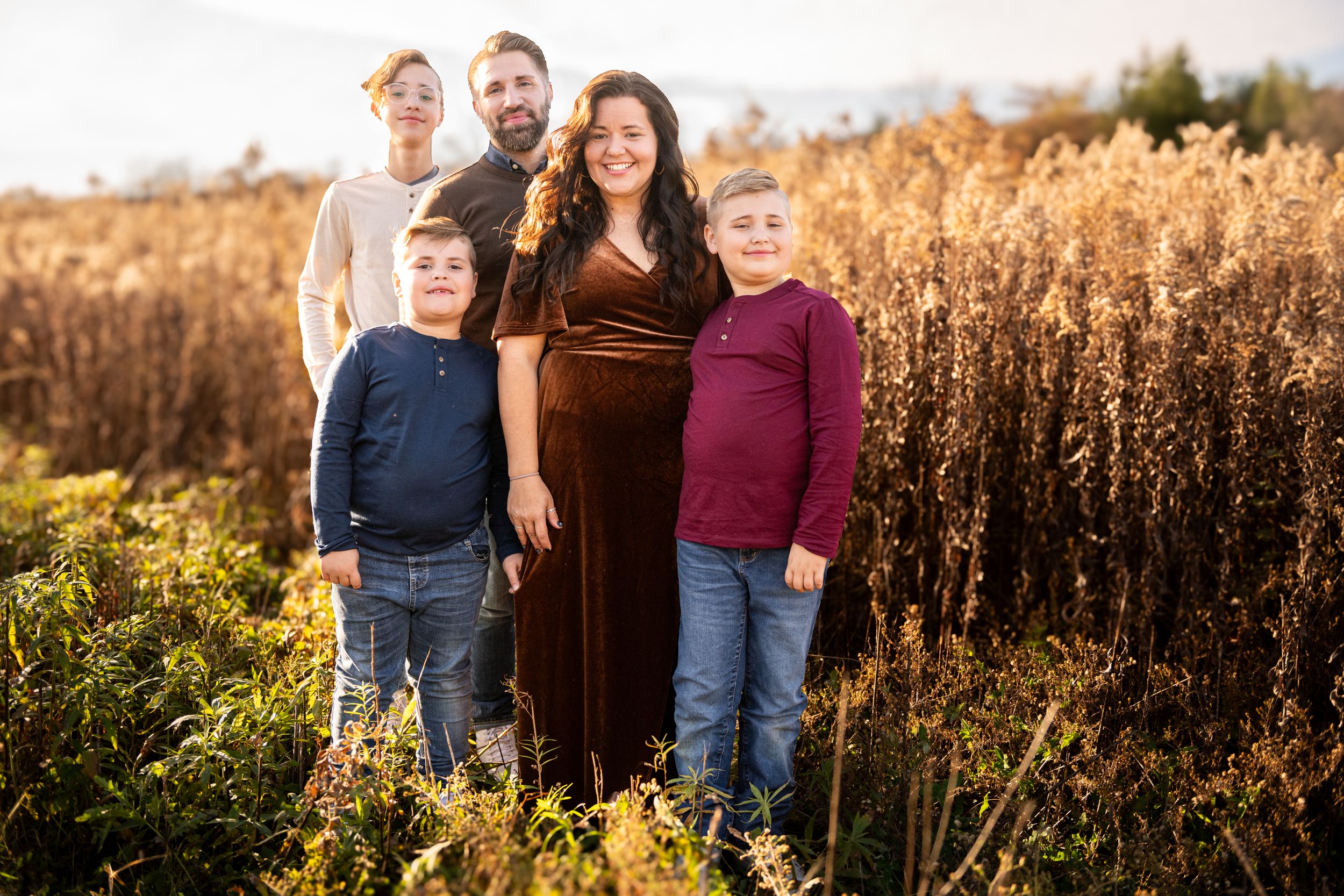 A family poses together in front of a golden field of tall grass during sunset.