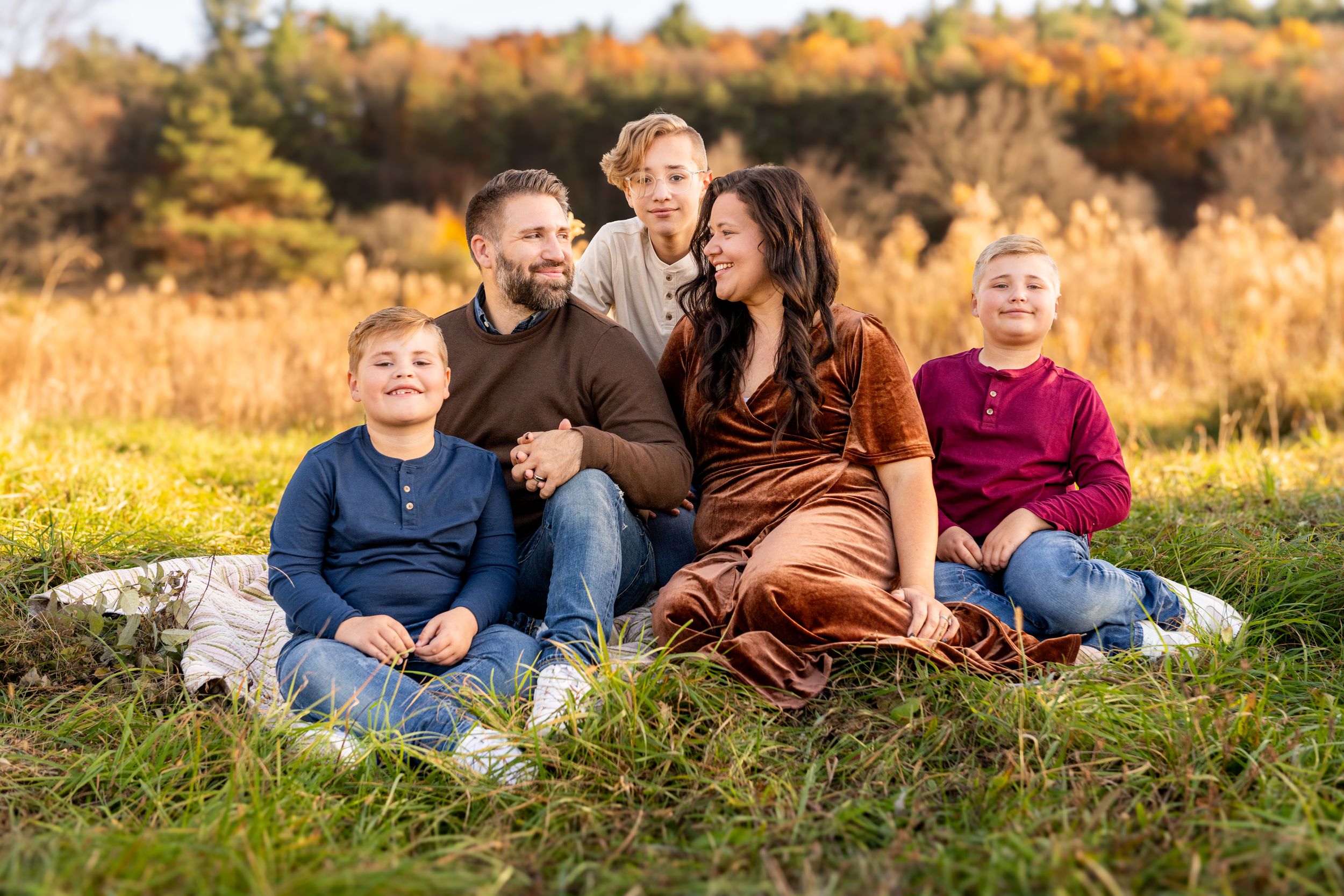 A family sits together on grass during autumn with golden foliage in the background.