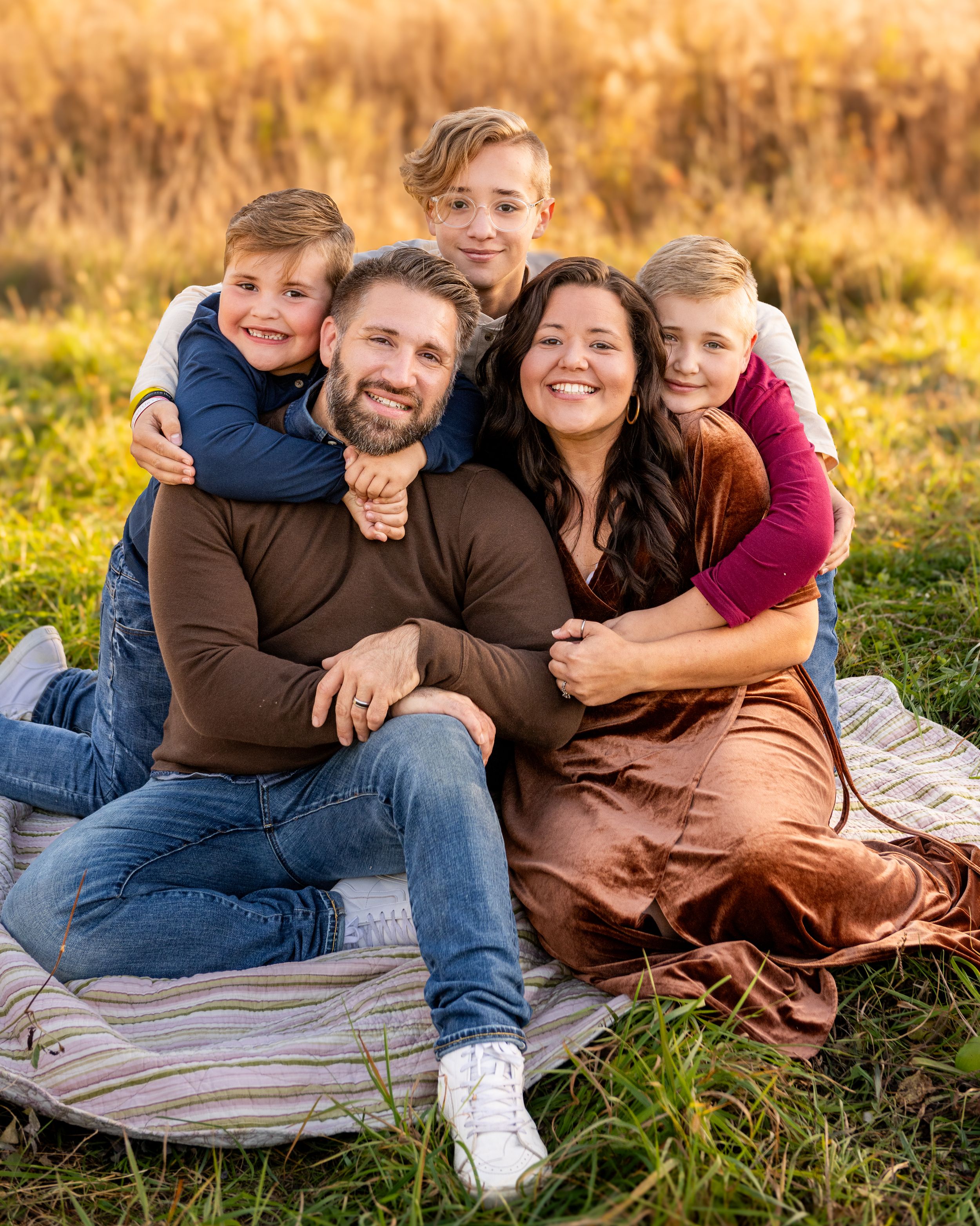 A family sits together on a blanket outdoors in autumn golden light sharing warm embraces.