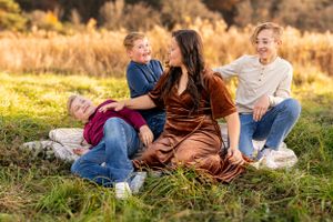Group sitting and laughing together on grass during golden hour with autumn foliage in background.