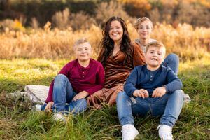 A small group sits together in a field of tall golden grass during sunset, smiling at the camera.