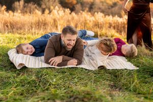 Family relaxes together on blankets in golden autumn field during sunset.