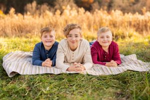 Three youths lie on a striped blanket in a grassy field during golden hour with warm autumn colors in background.