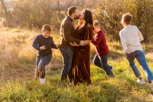 Family enjoying a playful moment together in a sunlit field during golden hour with children running around them.