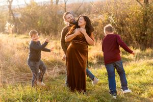 A family embraces in joyful moments outdoors during golden hour with sunlit trees and grass in the background.