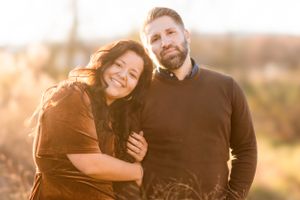 A couple embraces outdoors during sunset with warm autumn colors in the background.