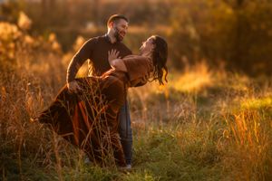 A romantic couple dances in a golden sunlit meadow during sunset while wearing casual and formal attire.