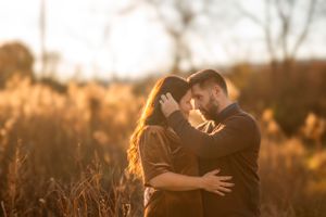 A romantic couple embraces in a field at sunset with golden sunlight creating a warm glowing atmosphere.