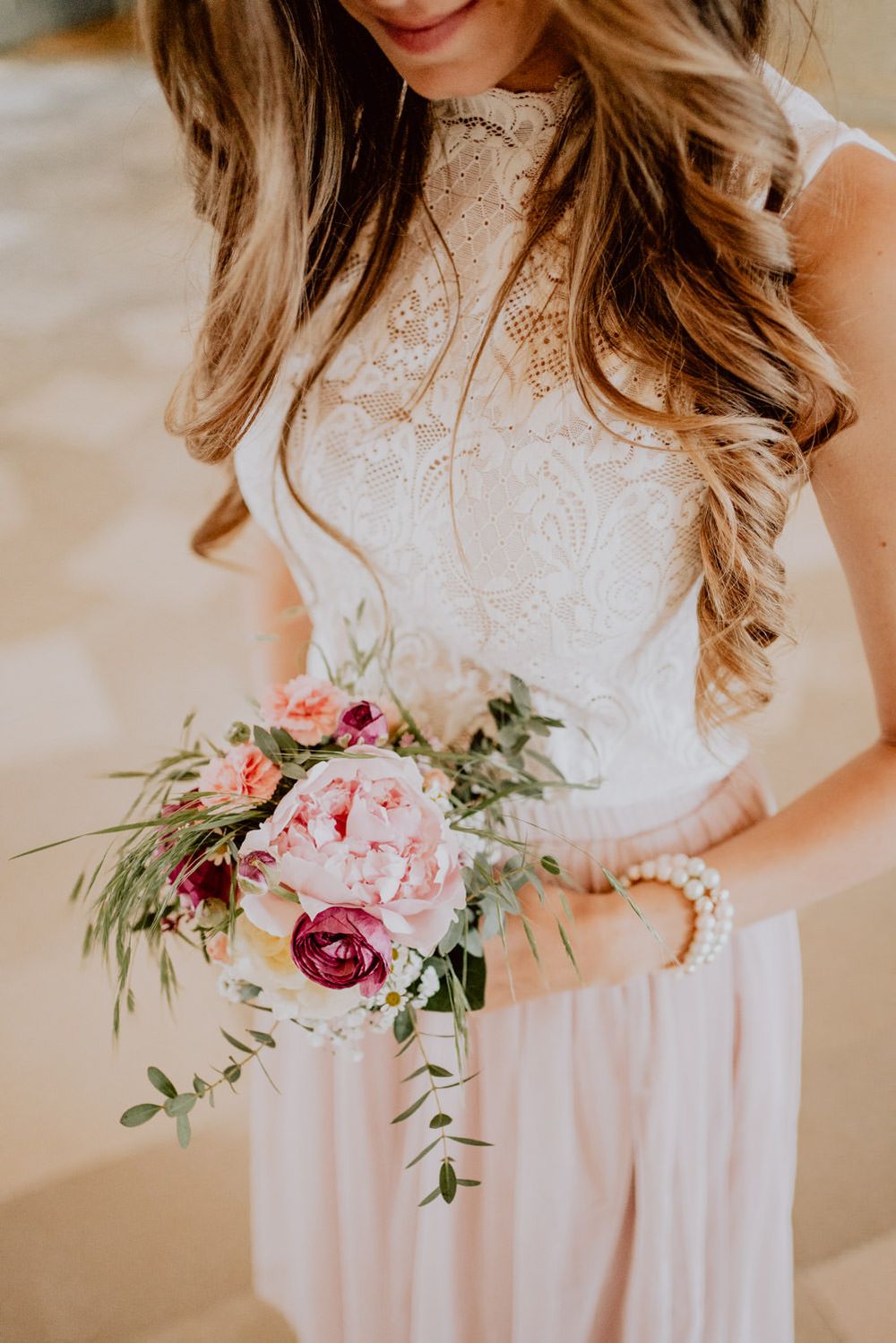 Detailed shot of lace wedding dress bodice with delicate bouquet featuring pink and burgundy blooms.