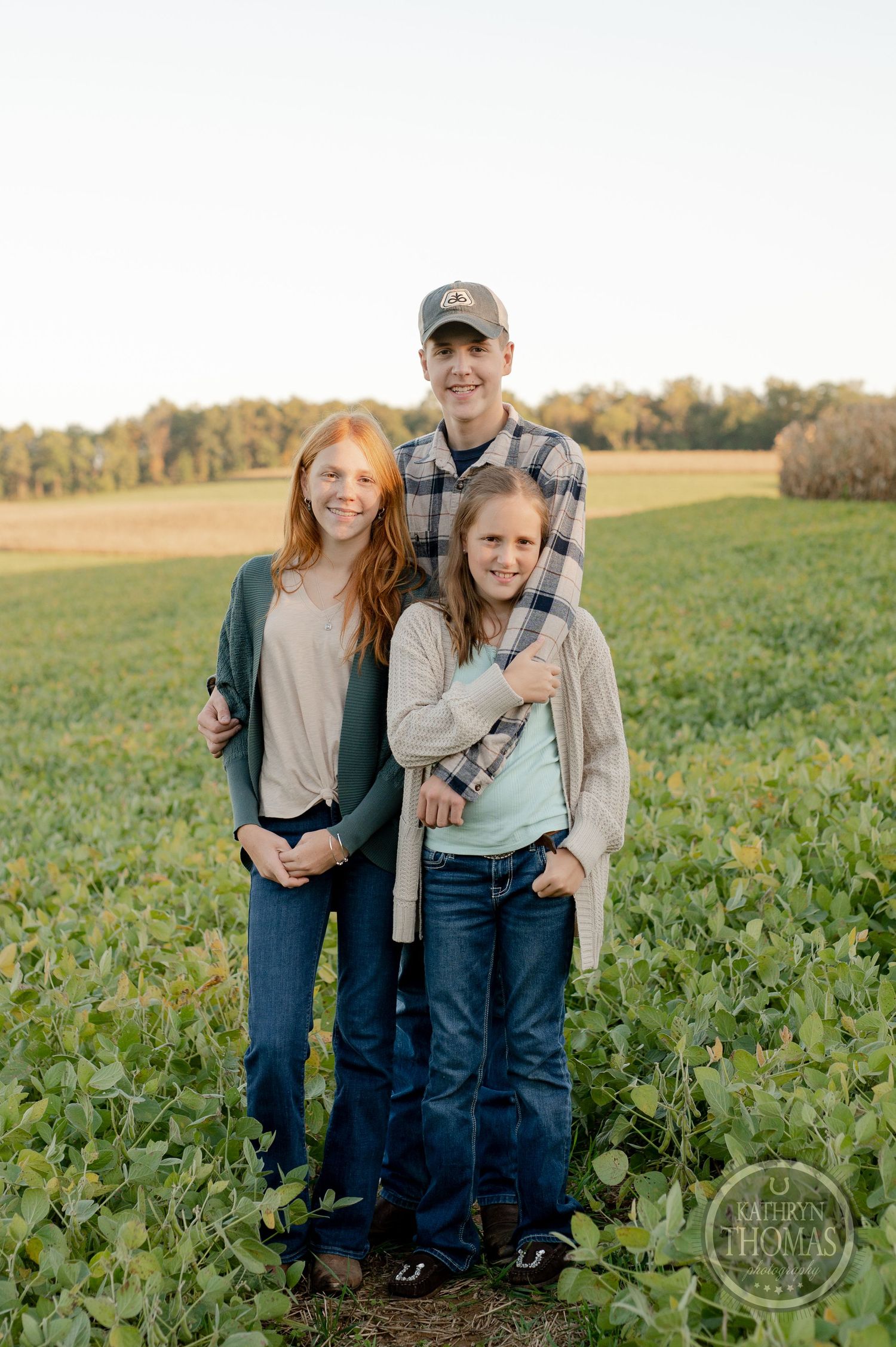 Three people stand together in a green agricultural field during golden hour.