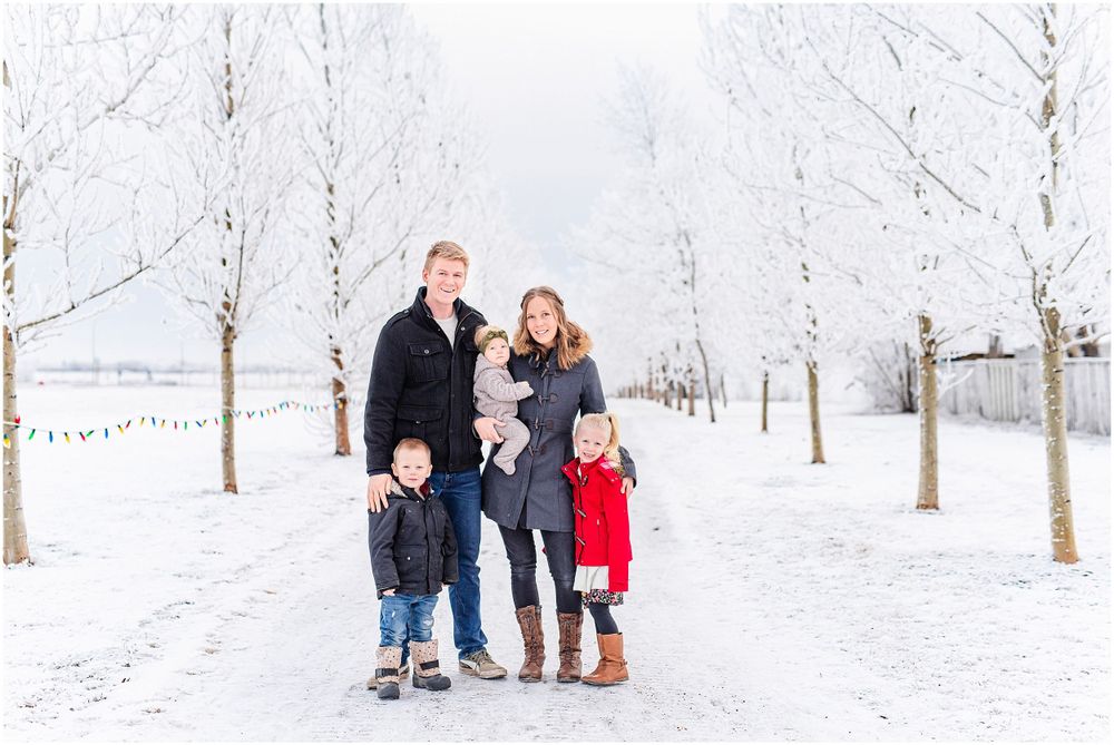 Family portrait in a snowy winter landscape with trees lined along a pathway.